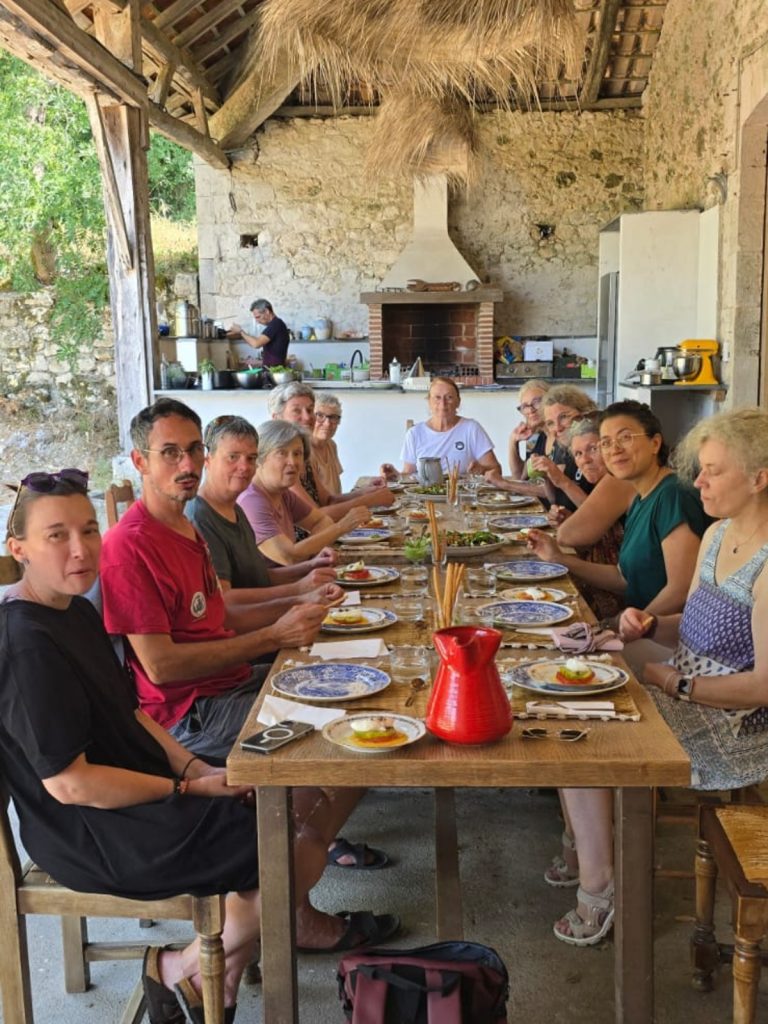 Participants de la retraite réunis autour de la table pour le repas, cuisine extérieure en arrière-plan