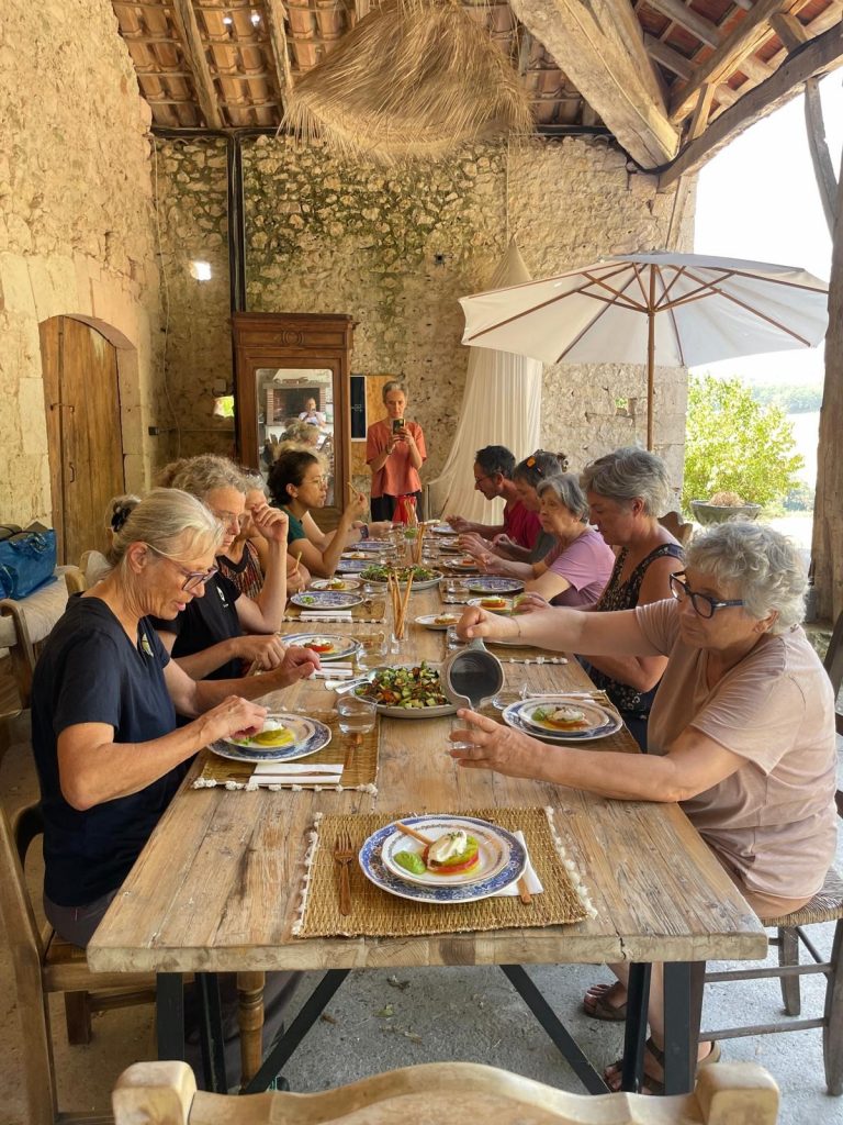 Participants de la retraite partageant un repas à table, sous la charpente en pierre du gîte